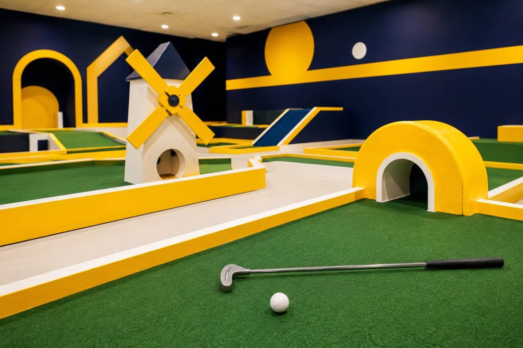 Parcours de mini-golf intérieur couvert avec obstacles colorés, club et boule blanche au premier plan